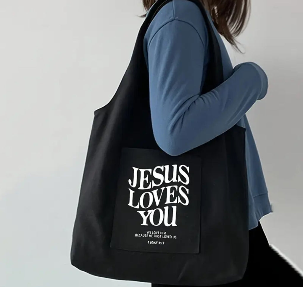 A person wearing a blue shirt carrying a black tote bag with the text 'JESUS LOVES YOU' printed on the back.