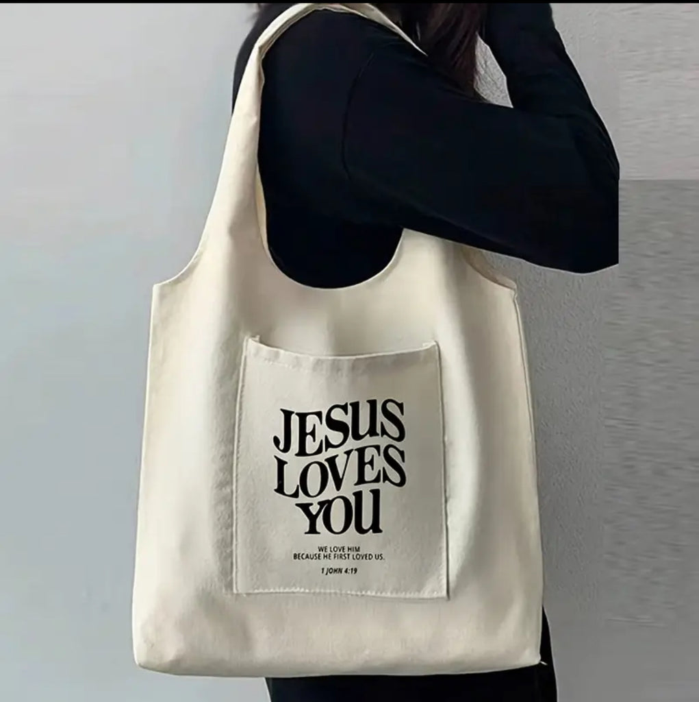 A person wearing a blue shirt carrying a black tote bag with the text 'JESUS LOVES YOU' printed on the back.
