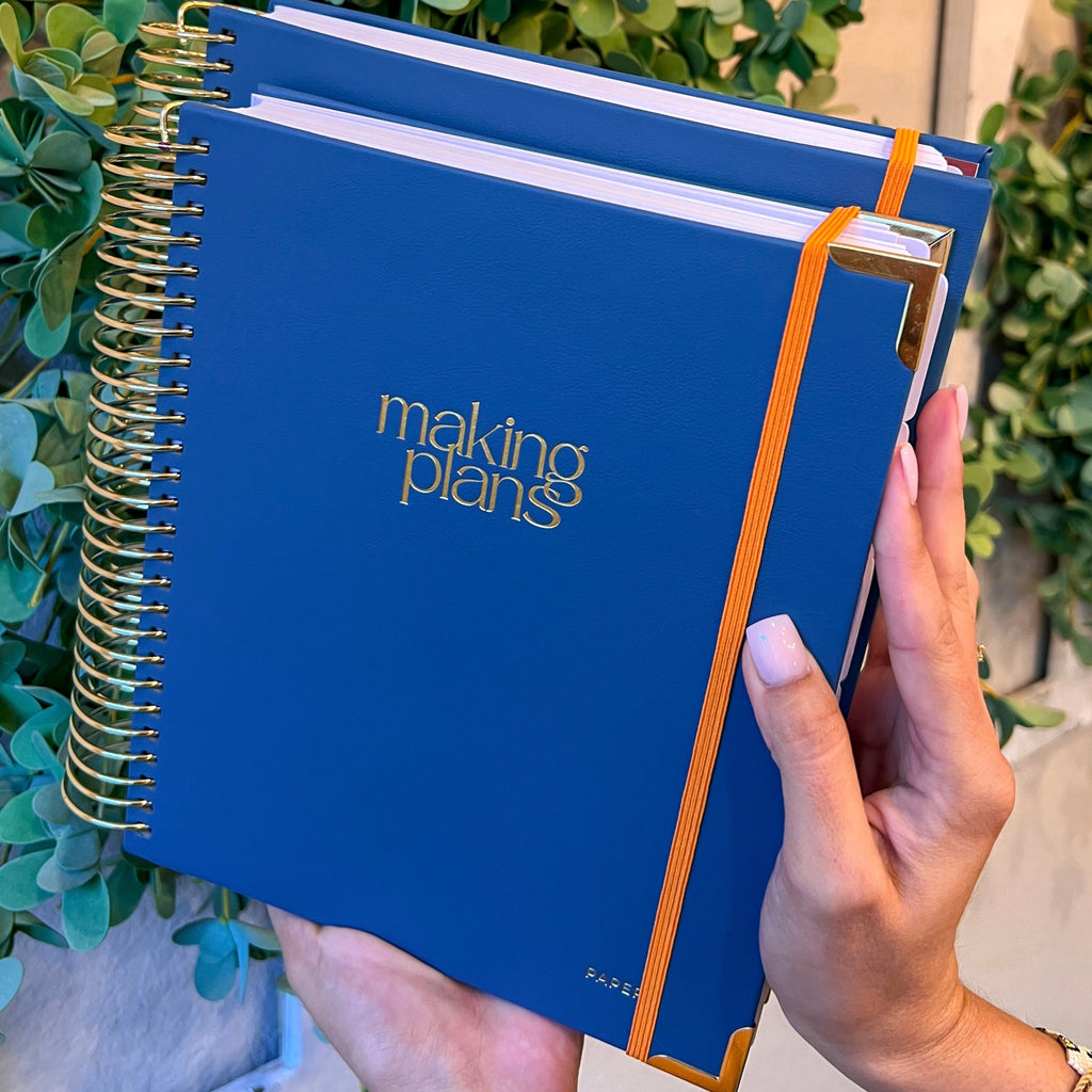 Blue notebook with 'making plans' text held by a hand against a green leafy background